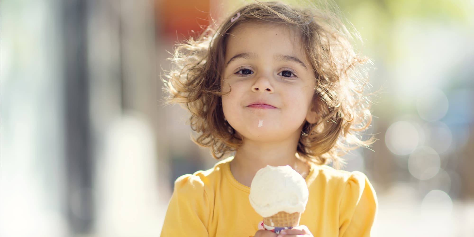 Little girl in yellow shirt eats vanilla ice cream on a cone