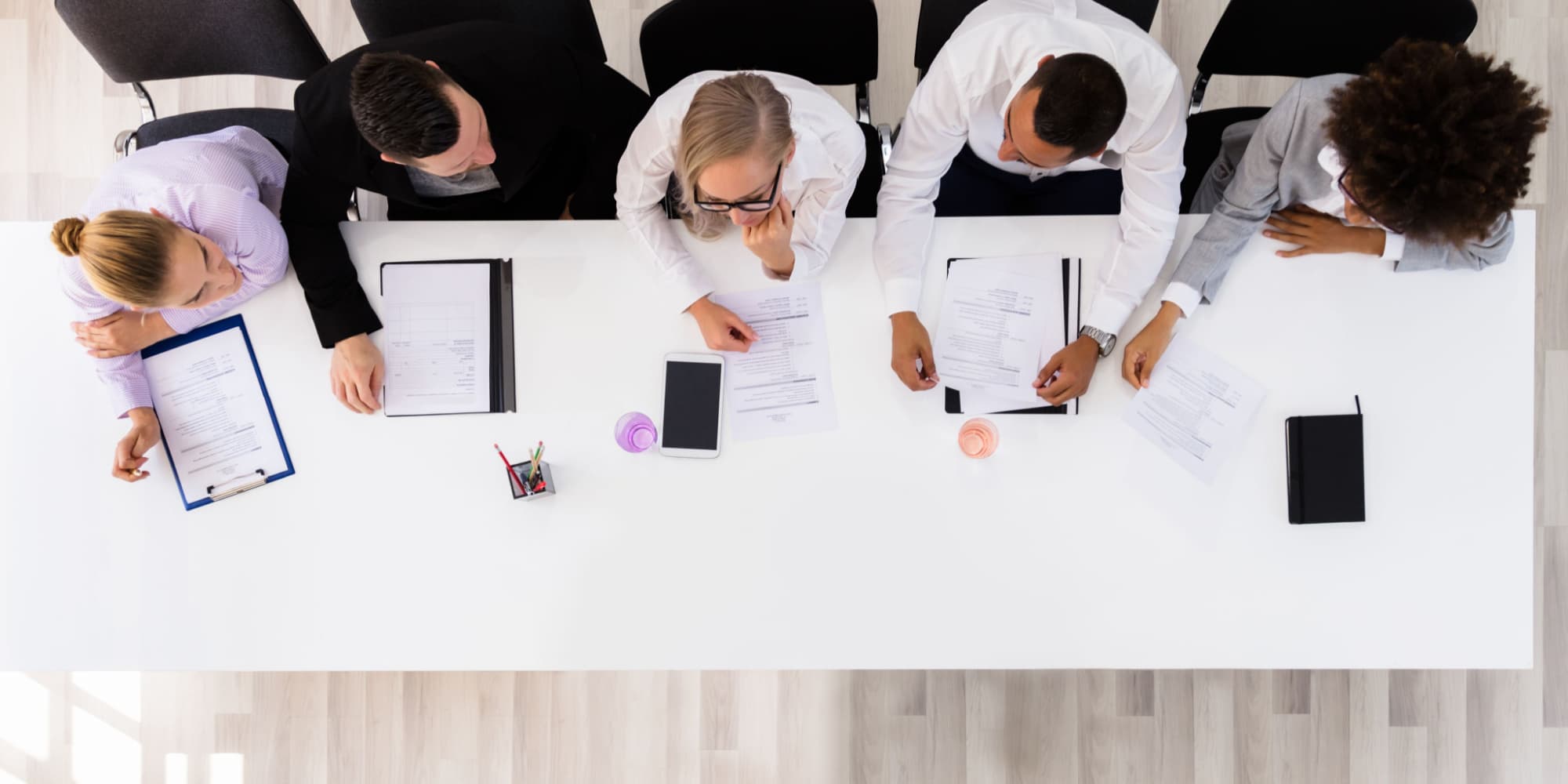 Five people sit at a white rectangular table viewed from above 